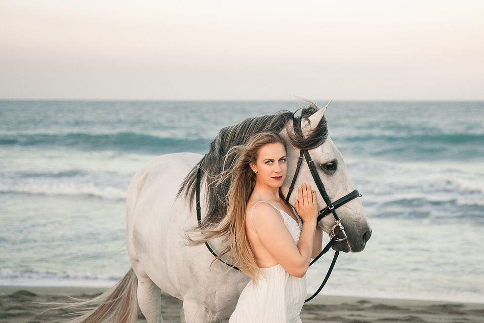 a portrait of a blonde girl wearing a white dress standing next to her grey andalusian gelding on the beach in Florida