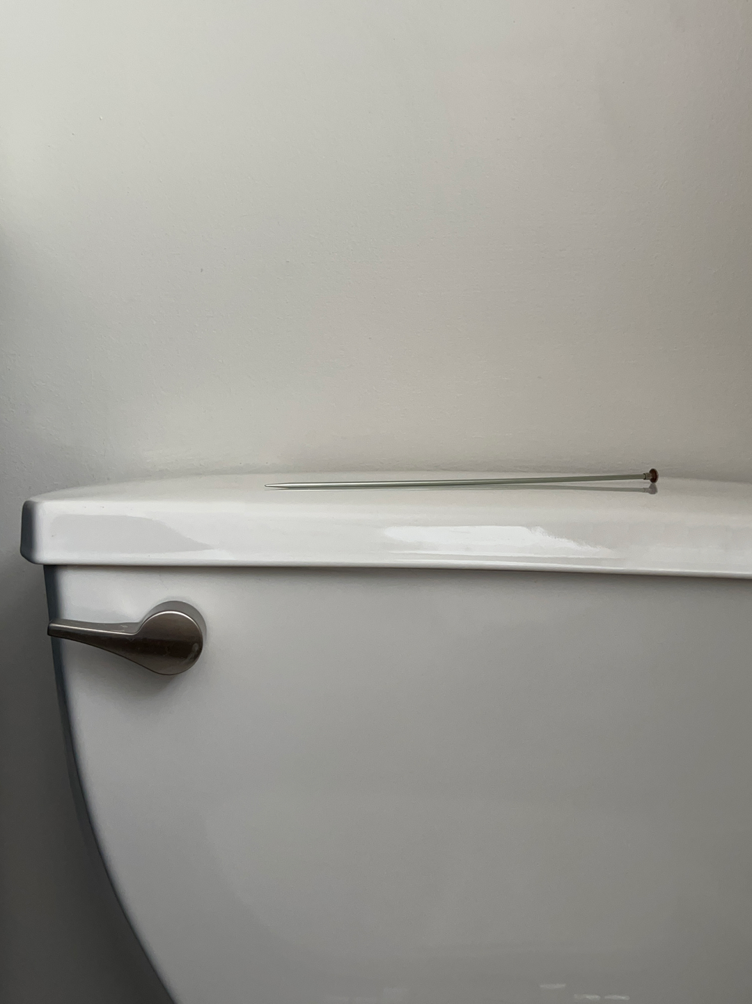 knitting needle on the top of a toilet