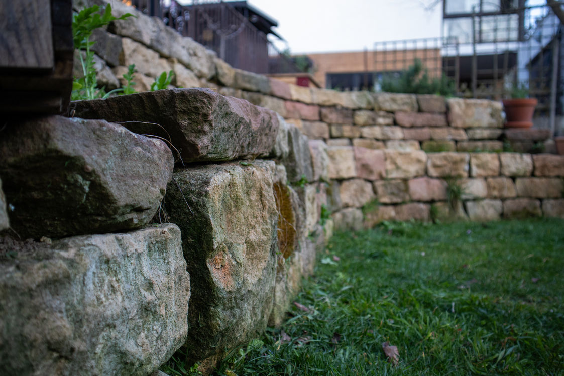 Projekt Natursteinmauer im privaten Garten als Sitzmöglichkeit und Stufe zur Gestaltung zweier Ebenen