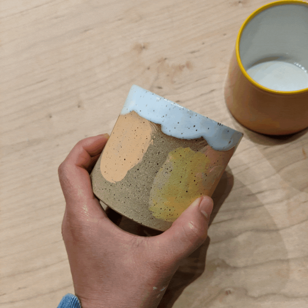 Handmade ceramic cup made with recycled, speckled clay with abstract brushstroke patterning around the body and a unique, white interior and petal-like boarder