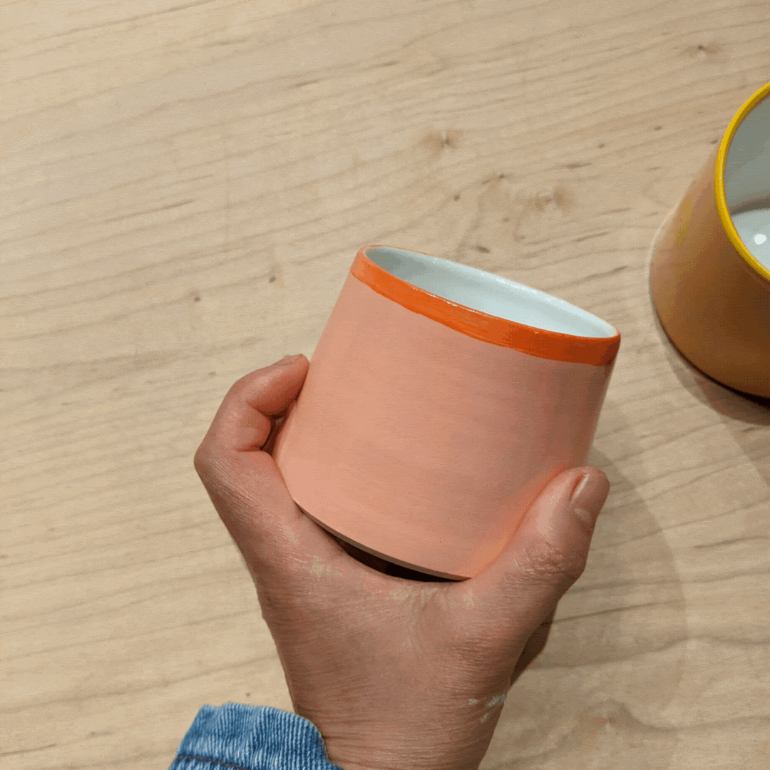 Handmade ceramic cup painted orange with decorative floral elements that wrap around the vessel in orange and dark navy.