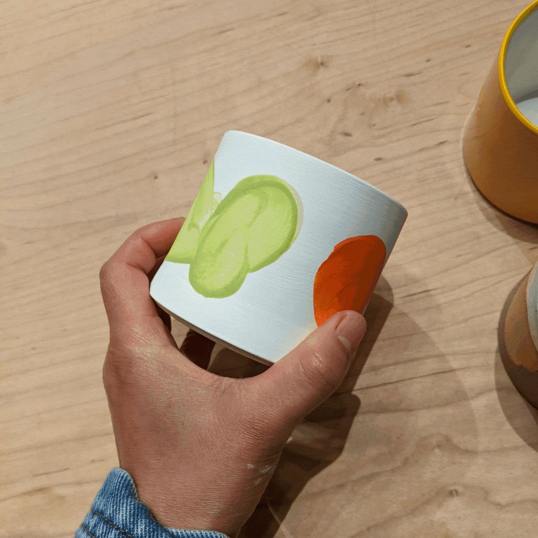 Handmade ceramic white cup with orange and green decorative elements that are reminiscent of abstract flora
