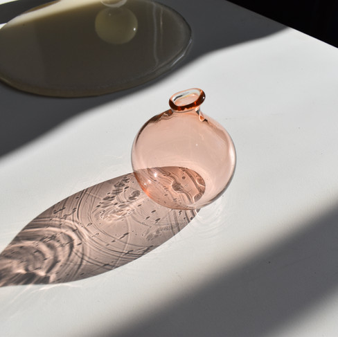 Lompie vase in a transparent peachy pink color. The reflection from the sunlight is imparting the reflections of bubbles and tool marks within. 