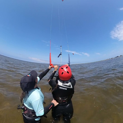 Instructeur de Plein Vent les îles tenant l'élève par le harnais et l'aidant à piloter la barre de kitesurf dans l'eau peu profonde aux Îles-de-la-Madeleine.