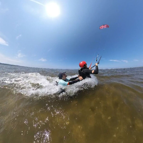 Élève de Plein Vent les îles effectuant un exercice de nage tractée sous le vent, glissant sur l'eau pendant que l'instructeur l'accompagne en te tenant par le harnais.