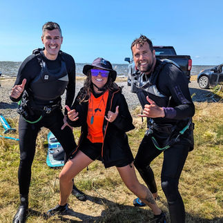 Deux hommes souriants après leur cours de kitesurf en duo, posant avec leur instructrice de Plein Vent les îles.