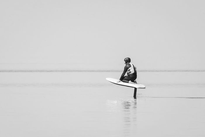 Débutant en position à genoux sur une planche d’e-foil apprenant à contrôler la manette et son équilibre pour s’élever au-dessus de l’eau.