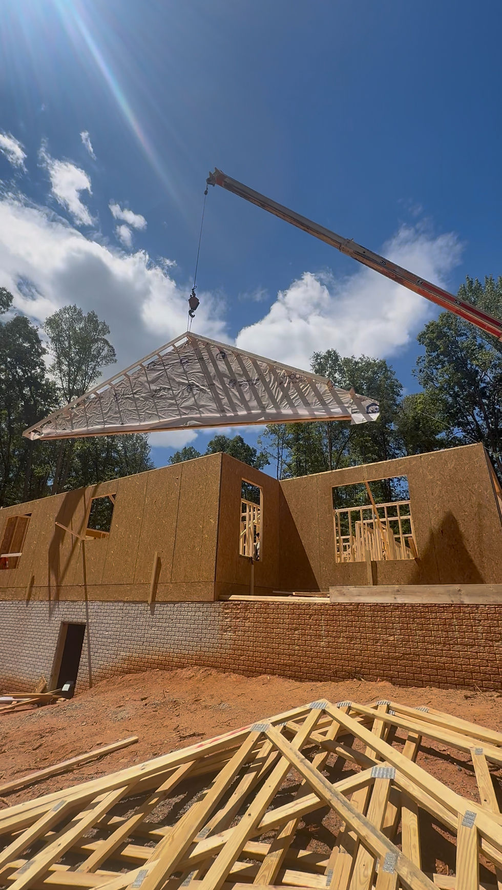 Crane lifting roof truss over framed house