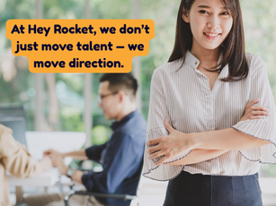 Smiling woman in office setting with arms crossed. Two blurred colleagues in background. Greenery outside. "Hey Rocket" logo in the top left corner and text: "at Hey Rocket we dont just move talent, but we move direction".