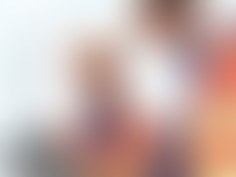 Two construction workers in orange vests and helmets review a tablet. They stand in front of a tall building, focused and engaged.