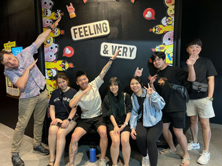 “Group of team members striking fun poses at a playful ‘Feeling & Very’ backdrop while exploring Melaka.