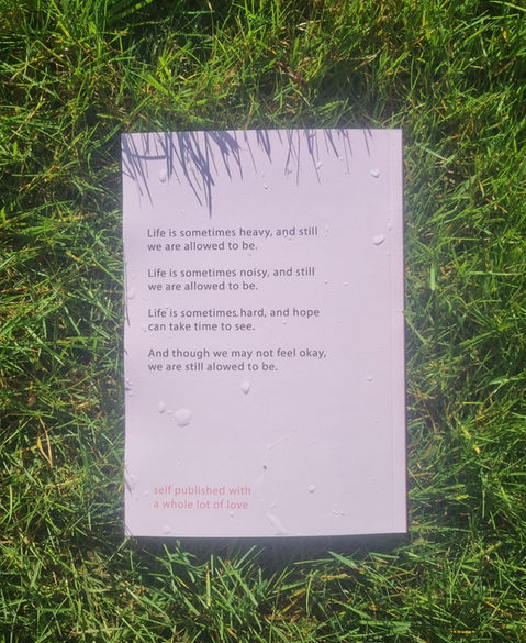 The back cover of the book "we are allowed to be okay" that is pink and reads "life is sometimes heavy, and still we are allowed to be, sometimes life is messy and still we are allowed to be, life is sometimes hard, and hope takes time to see, and though we may not feel okay we are still allowed to be"