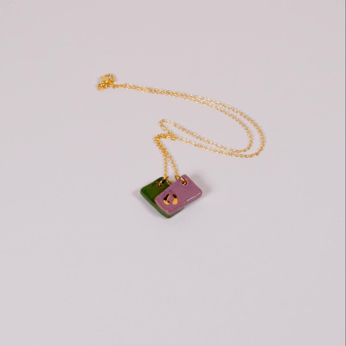 Zwei farbige Halsketten mit Anhängern auf weißem Hintergrund präsentiert.