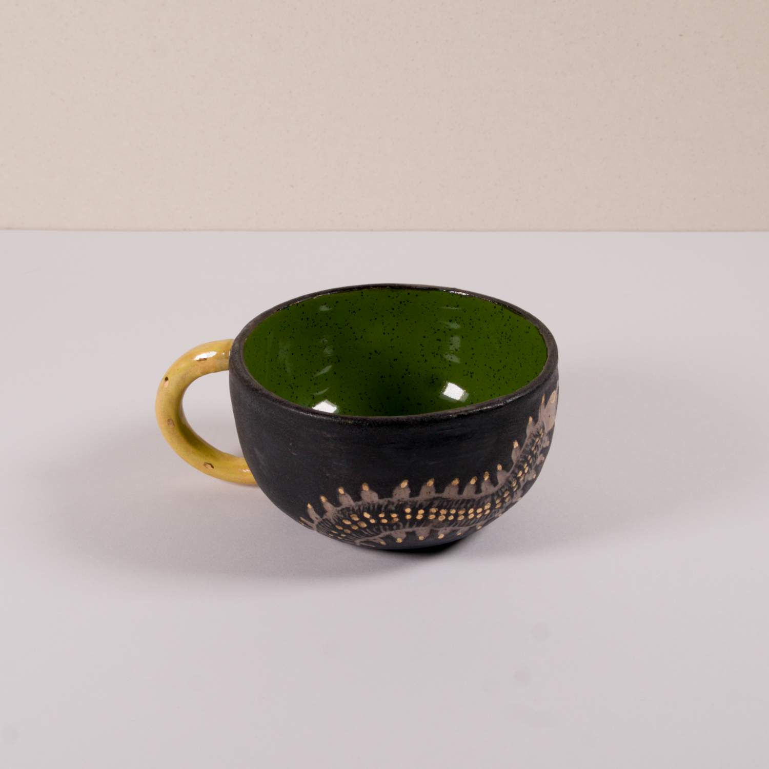Schwarze Keramik-Teetasse mit gelbem Griff und grünem Inneren auf Tisch.