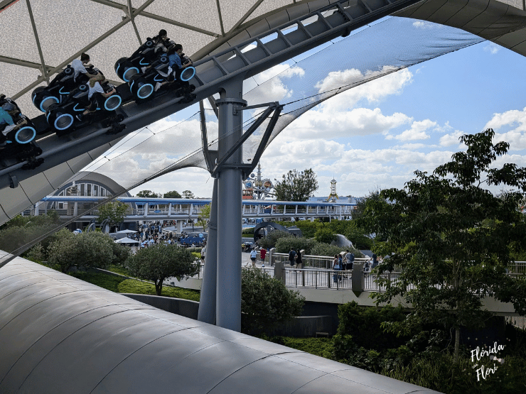 Montanha-russa TRON com motos iluminadas sob estrutura futurista no Magic Kingdom; céu azul e visitantes ao fundo