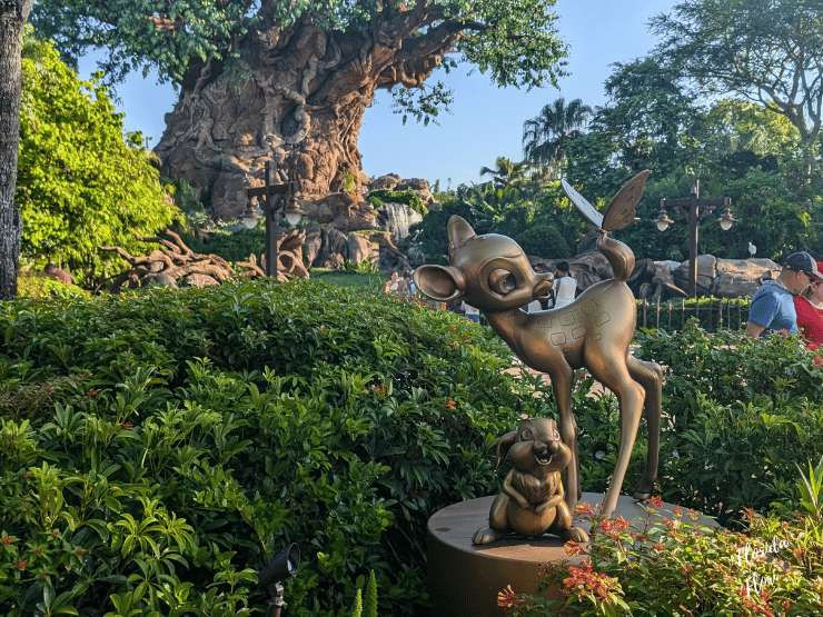 Estátua dourada do Bambi e coelho em jardim, com a Árvore da Vida no roteiro do animal kingdom. Céu azul e vegetação densa no Animal Kingdom em Walt Disney World