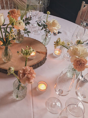 Bud vases as a wedding centrepiece with tealights candles with white roses, caramel carnations, feverfew, ornithogalum, ranunculus. Some on a wood log slice