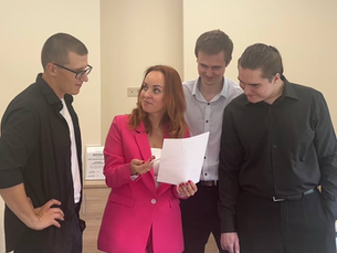 Трое людей стоят вокруг женщины, которая изучает документы.