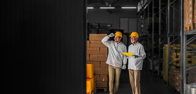 father-son-standing-their-warehouse-with-helmets-their-heads-looking-package-prepared-tran