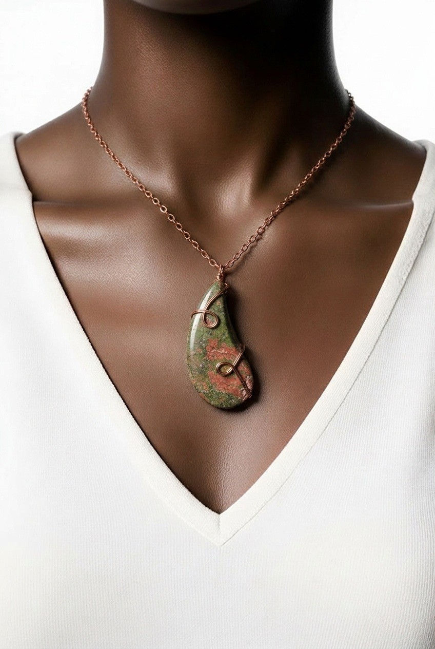 Handmade Unakite teardrop pendant wrapped in copper wire with decorative spiral accents on model