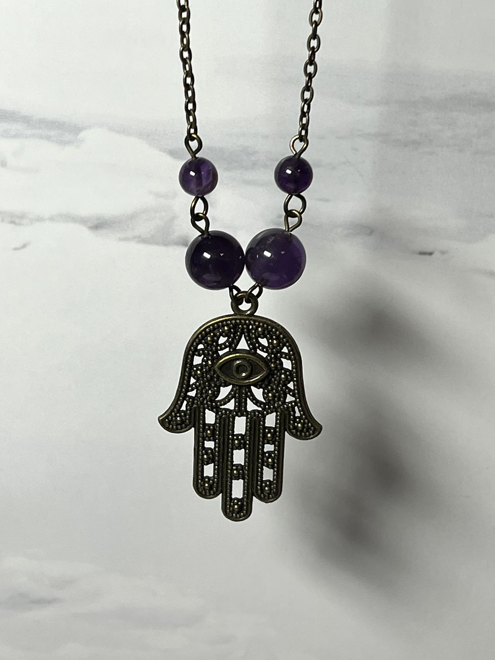 Thumbnail: Large bronze Hamsa hand necklace with two sizes of purple amethyst beads hanging from a bronze chain