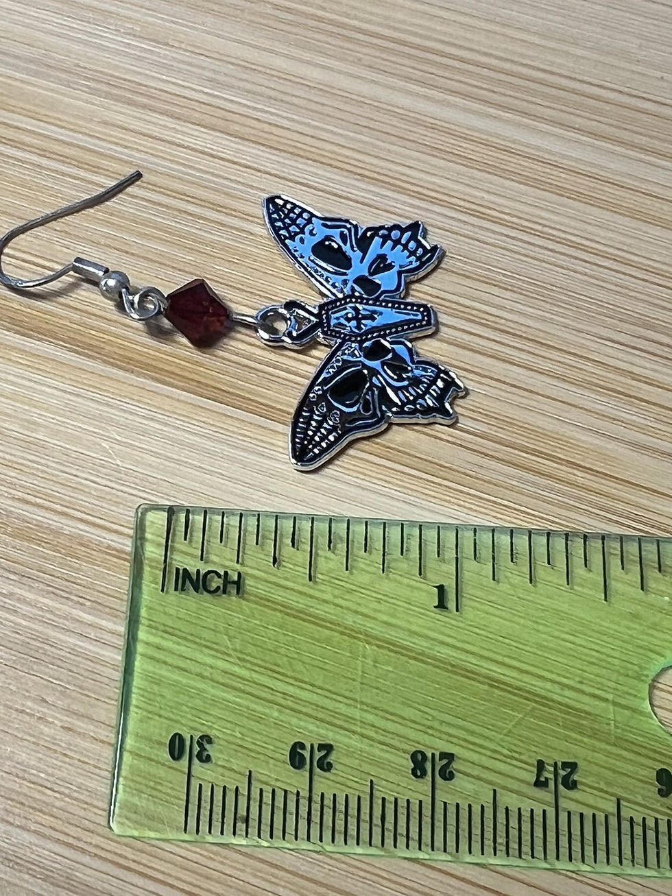 Thumbnail: Handmade gothic moth earrings featuring a coffin-shaped body, skull wing details, and red or black  bicone beads length