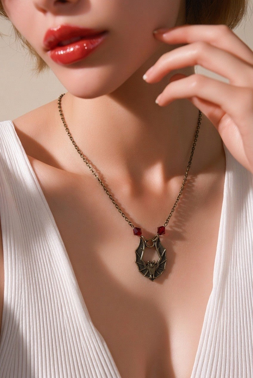 Gothic bronze bat necklace suspended from bronze chain with deep red crystal bicone on model