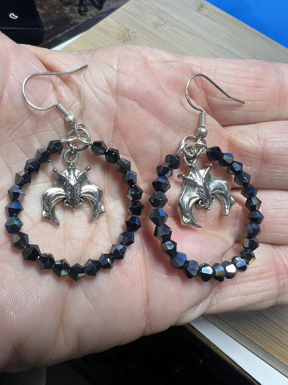 Thumbnail: Handmade hoop earrings made with black faceted bicone beads featuring a small bat charm suspended in the center in hand