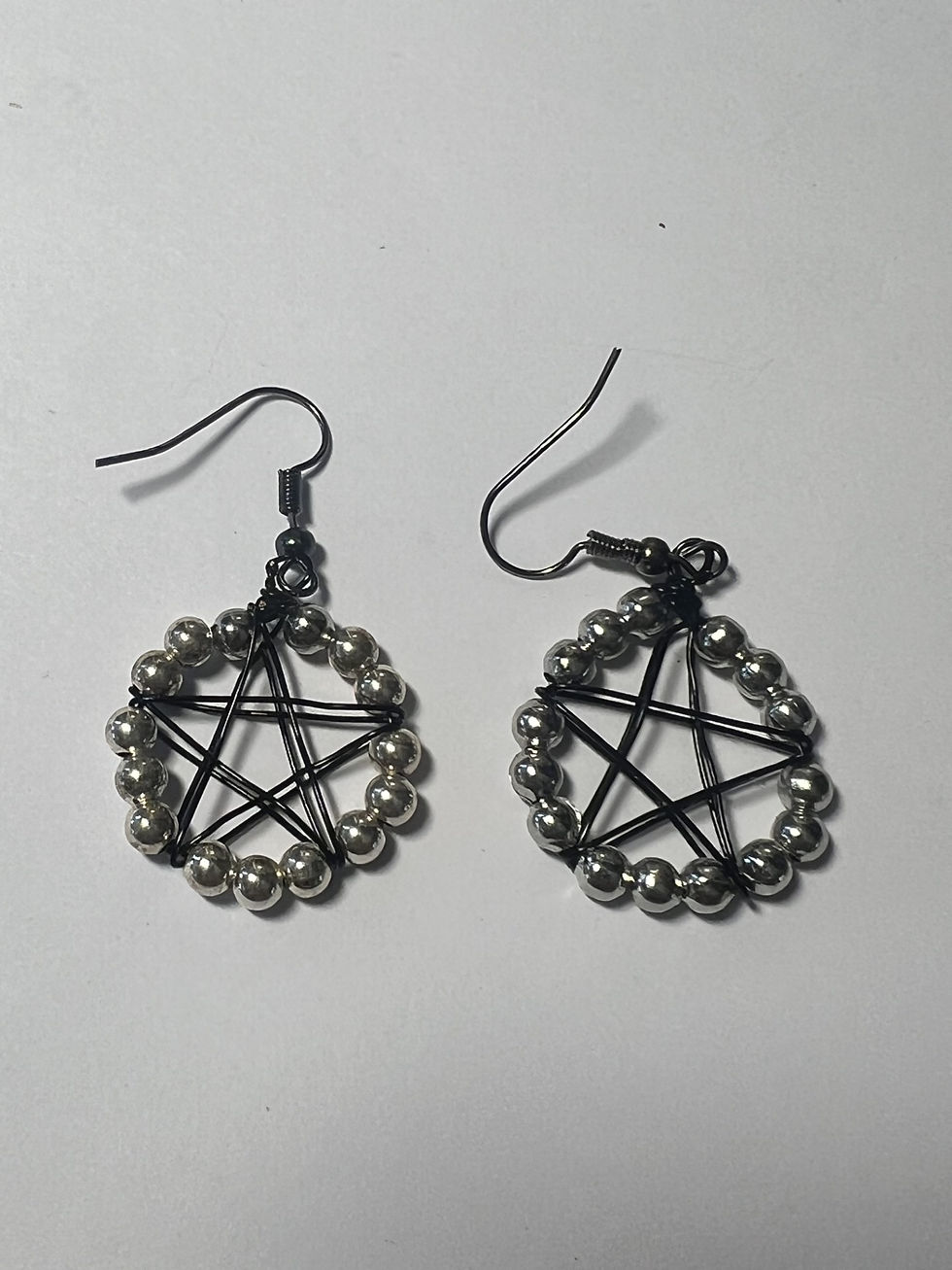 Thumbnail: Handmade black wire wrapped pentacle earrings with silver bead accents hanging from silver ear wires closeup