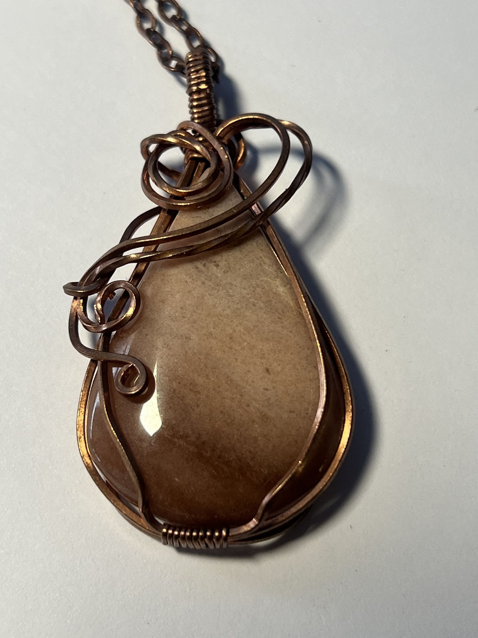 Thumbnail: Handmade calcite teardrop pendant wrapped in copper wire with decorative swirls closeup