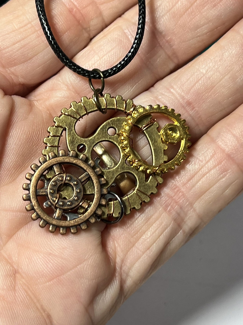 Thumbnail: Handmade steampunk necklace featuring a large bronze gear decorated with copper and gold tone gears in hand