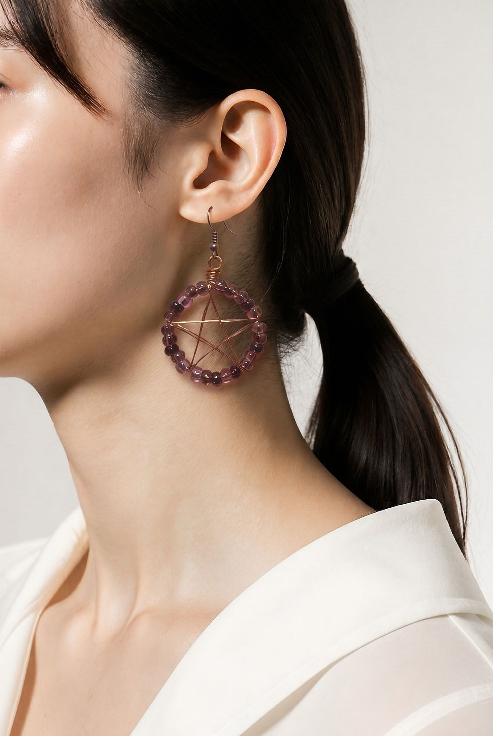Handmade copper wire wrapped pentacle earrings with purple bead accents in a mystical pagan style on model