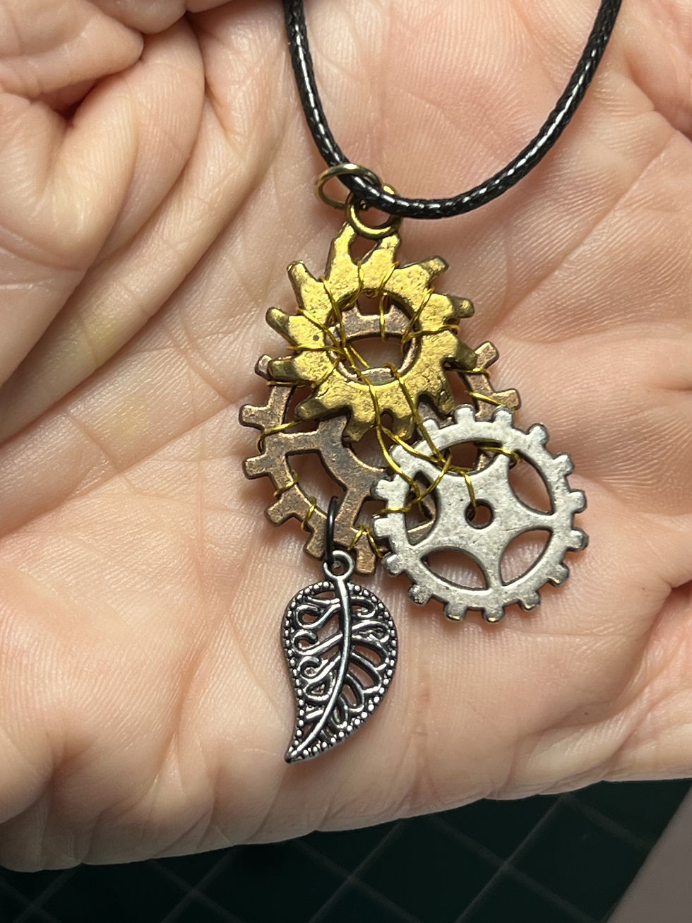 Thumbnail: Handmade steampunk necklace featuring a large copper gear layered with gold and silver tone gears and hanging leaf in hand