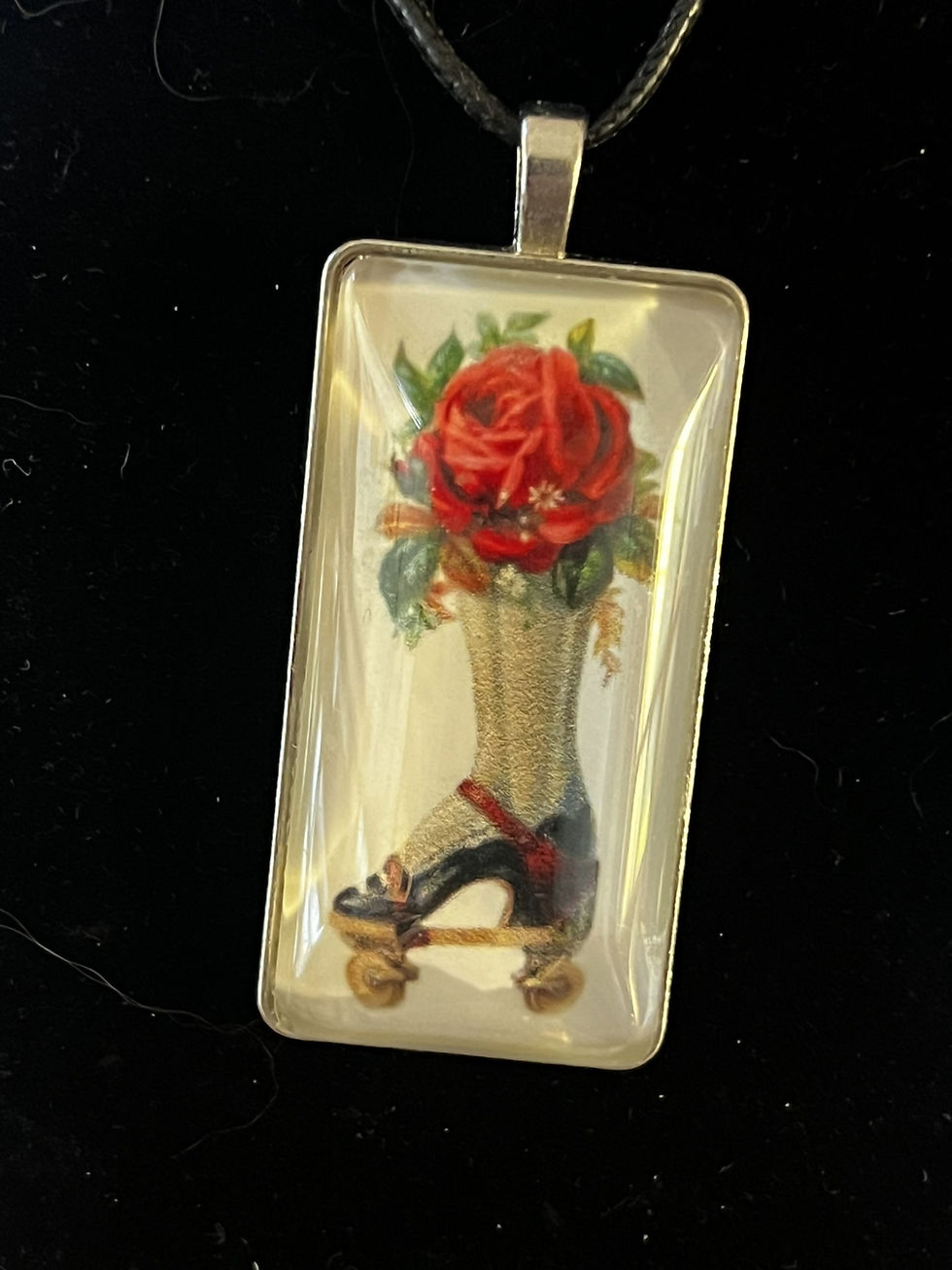 Thumbnail: Handmade cabochon necklace featuring a vintage roller skate with a rose nestled inside the skate opening