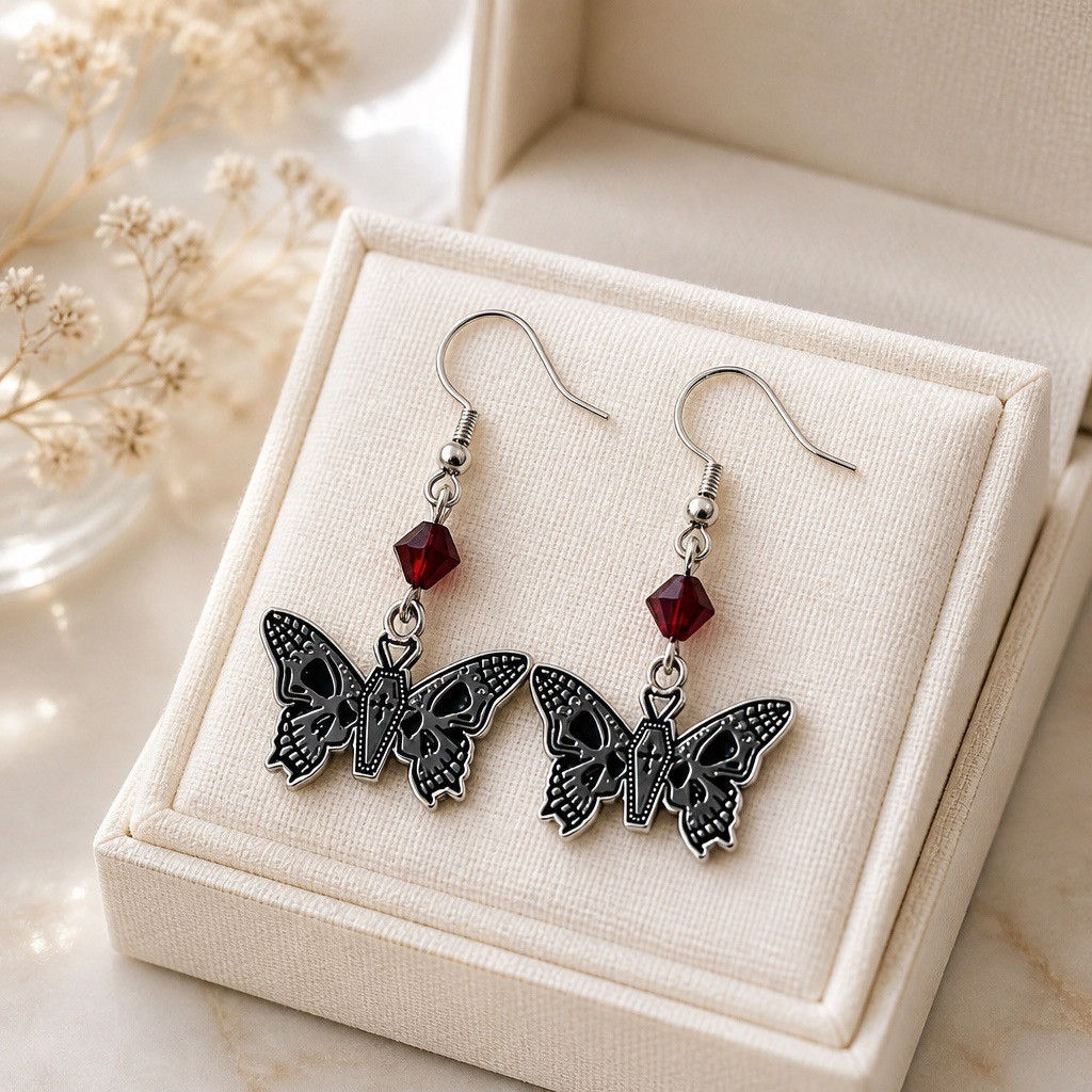 Handmade gothic moth earrings featuring a coffin-shaped body, skull wing details, and red or black faceted bicone beads