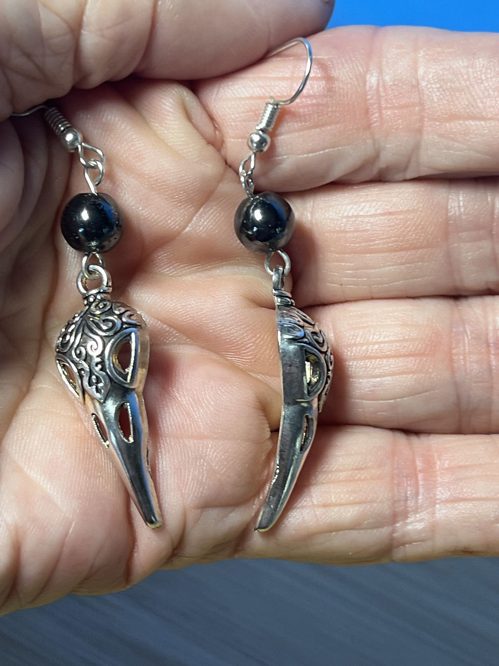 Thumbnail: Handmade silver raven skull earrings accented with polished hematite beads and gothic styling in hand
