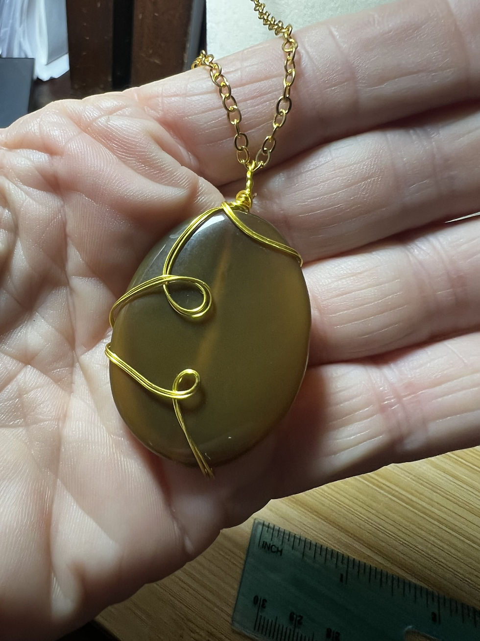 Thumbnail: Large oval Fire Agate pendant wrapped in gold-colored wire with decorative spiral accents in hand