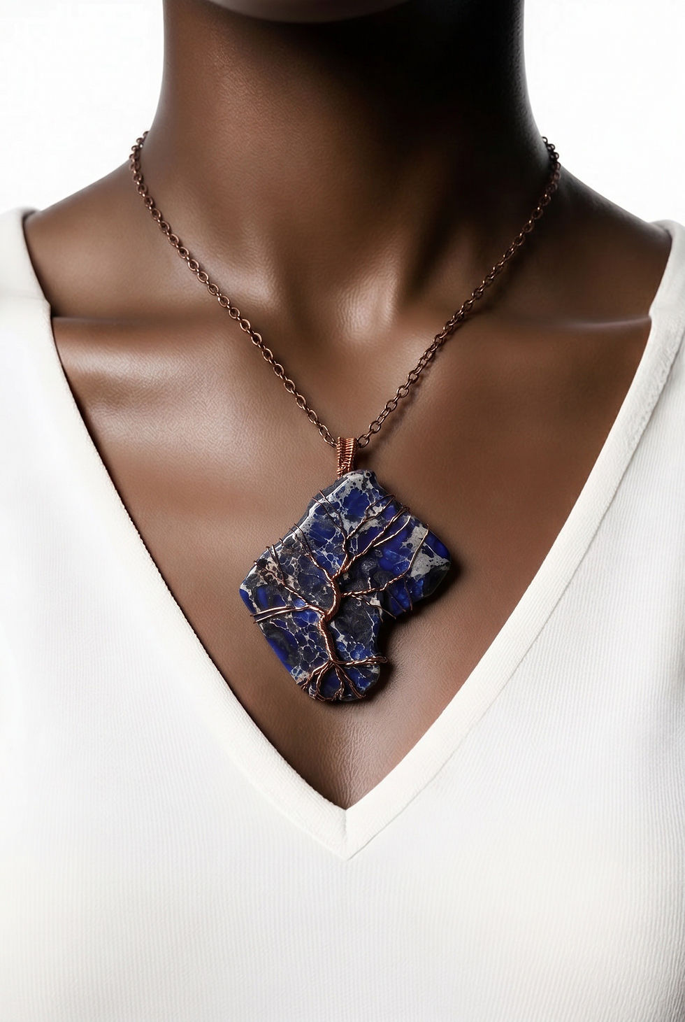 Thumbnail: Handmade dark blue jasper pendant in a unique freeform shape featuring an intricate copper wire Tree of Life on model