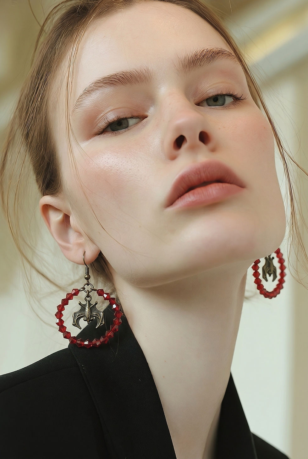 Thumbnail: Handmade hoop earrings made with red faceted bicone beads featuring a bronze bat charm suspended in the center on model