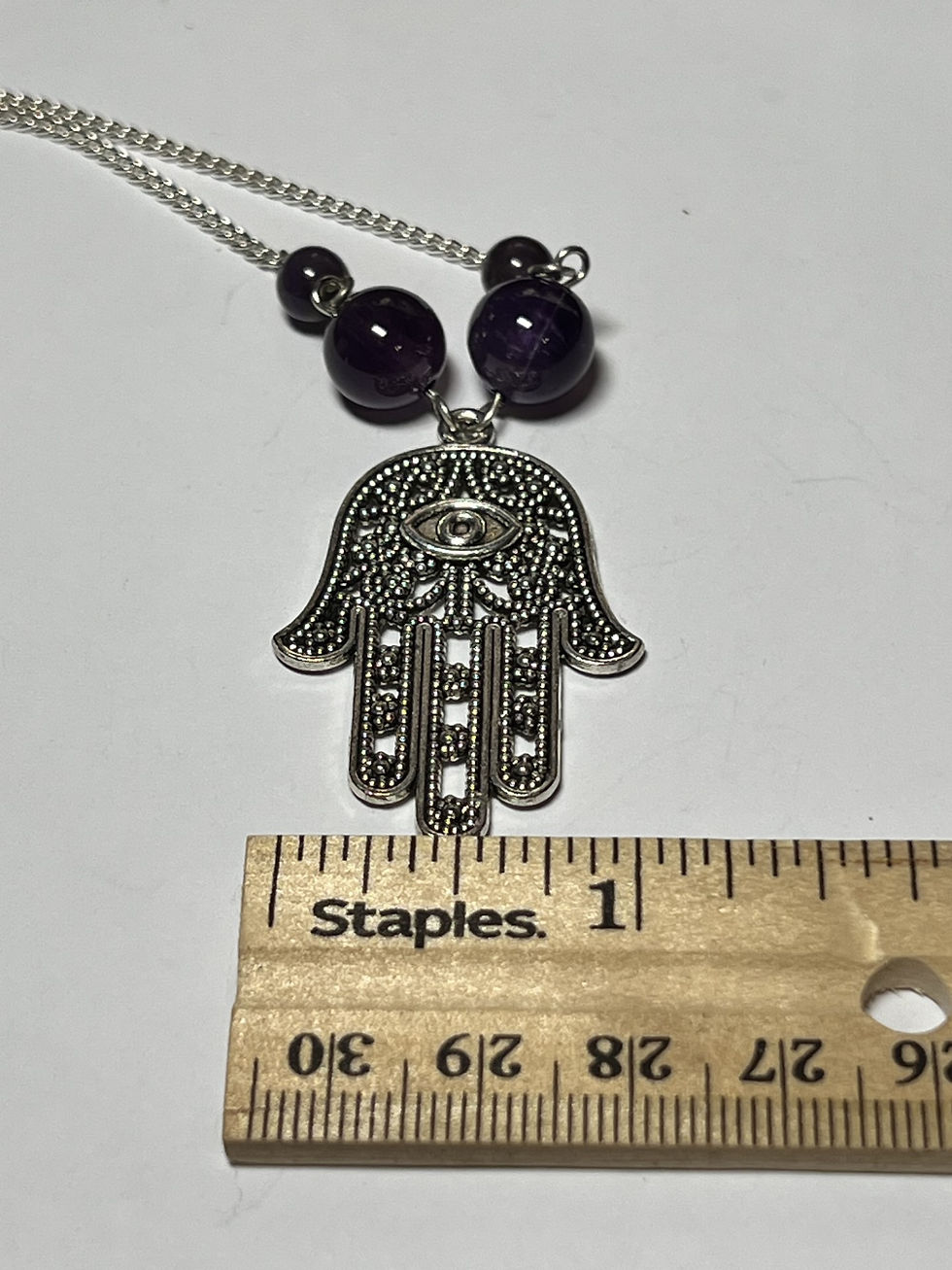 Thumbnail: Large silver Hamsa hand necklace with two sizes of purple amethyst beads hanging from a silver chain measure