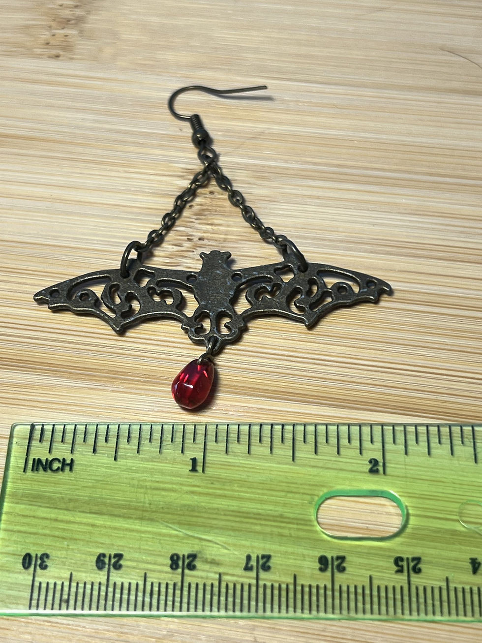 Thumbnail: Large bronze filigree bat earrings suspended from chains with dangling red or gold drop beads width
