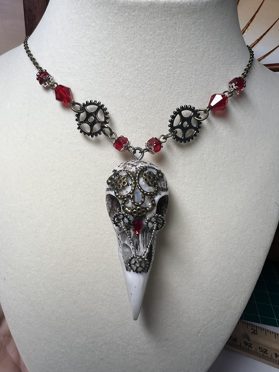 Thumbnail: Handmade steampunk necklace featuring a white raven skull pendant decorated with gears and a red jewel