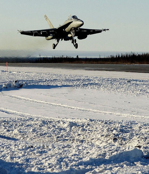 Jet coming in for a landing with the snow-covered ground surrounding the runway.