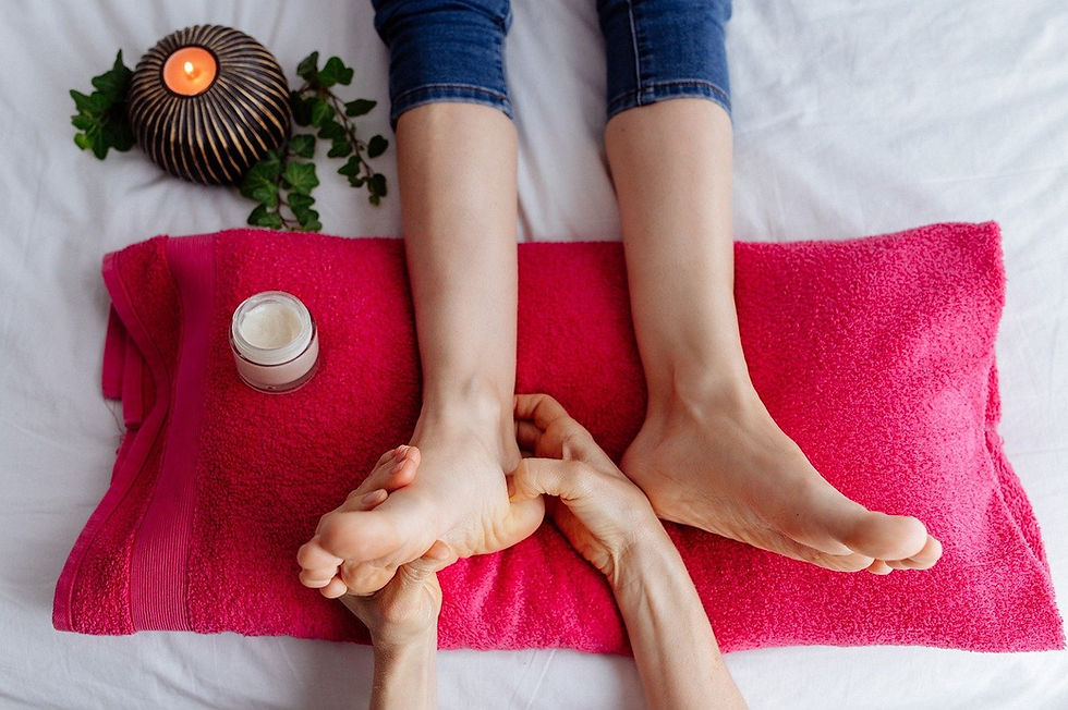 Feet being massaged on a vibrant pink towel, next to a candle and cream jar, creating a relaxed spa-like atmosphere.