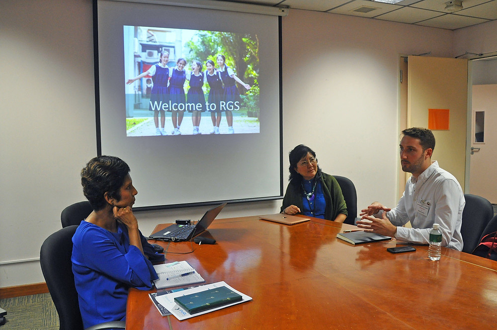 A meeting of three educations around a table. In the background is a PowerPoint slide with an image of the school.
