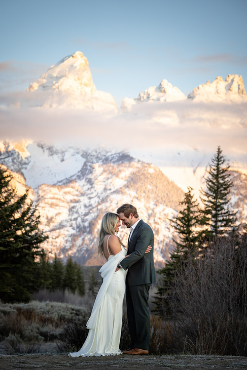 Bride and groom sharing a kiss and holding hands at sunrise at Schwabacher's Landing with alpenglow on the Grand Tetons