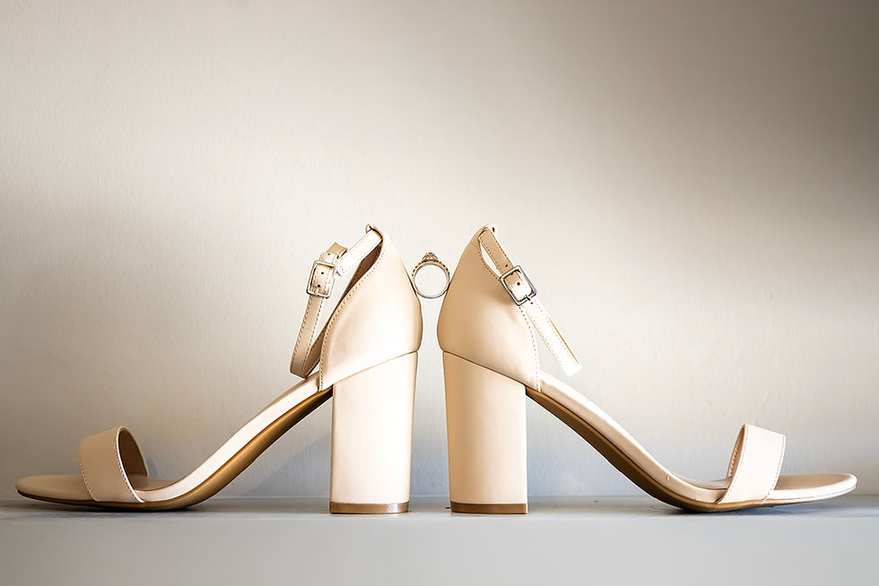 Beige high heels facing each other, a ring balanced between them on a neutral background, creating a minimalist and elegant scene.