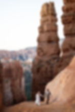 Couple in formal attire runs through red rock canyon under clear sky. They hold hands, creating a joyful, adventurous mood.