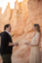A man and woman smiling at each other, exchanging notebooks in a desert setting with tall orange rock formations, suggesting a warm mood.