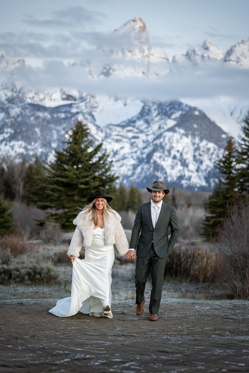 Bride and groom holding hands at sunrise at Schwabacher's Landing with alpenglow on the Grand Tetons